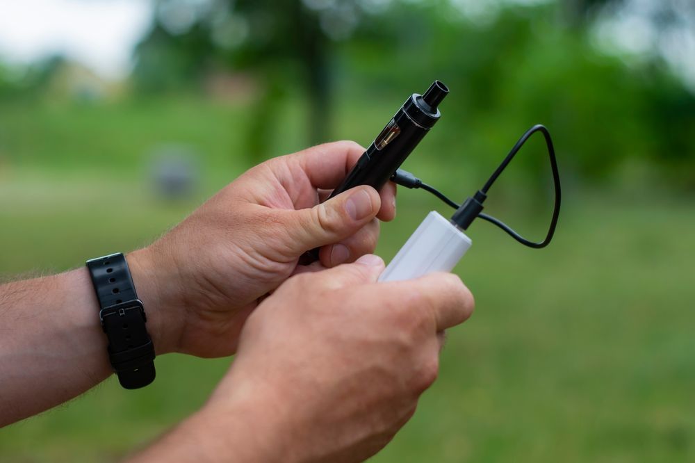 A man is charging his vape battery using a powerbank, outdoor setting