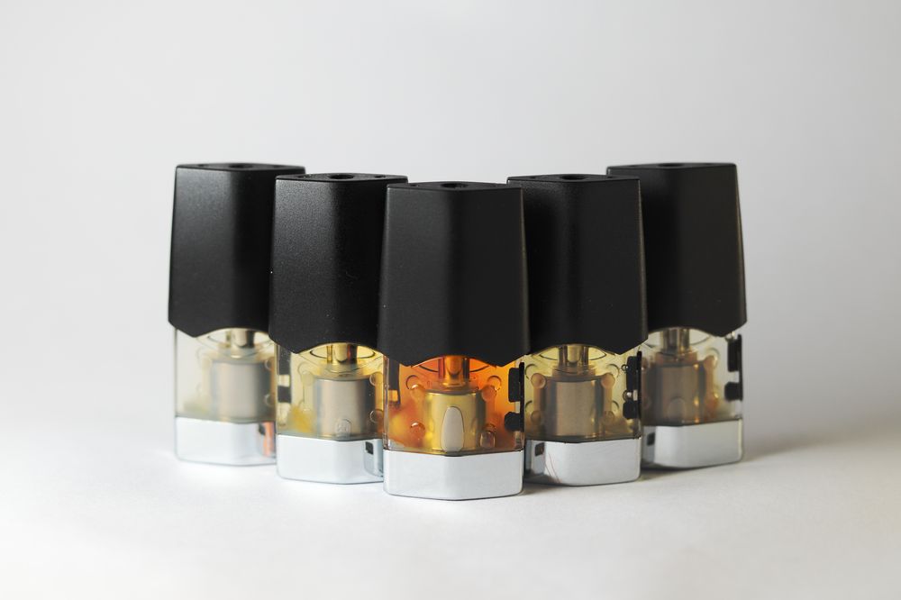 Five disposable vape pods are arranged on a white surface
