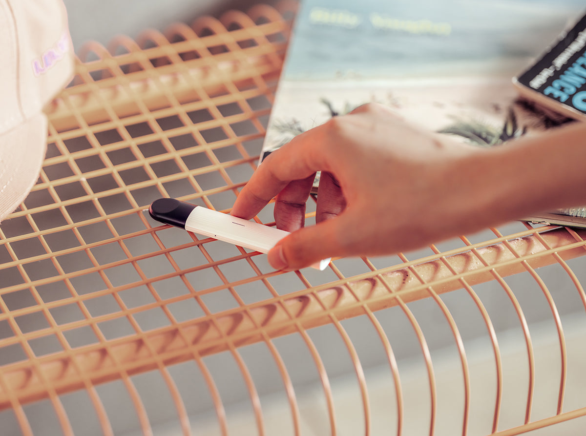 White RELX Essential device on a wire bench being placed by a hand