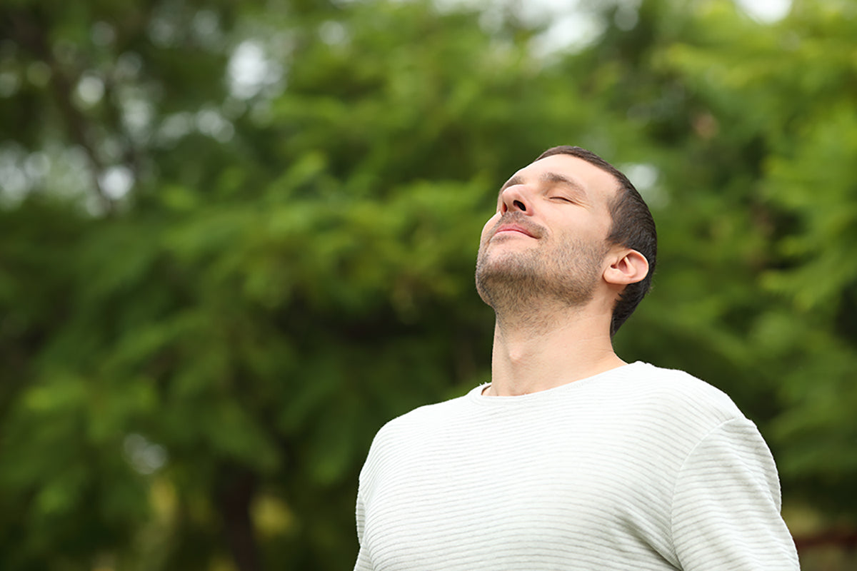 Man breathing fresh air in a forest with green trees in the background.