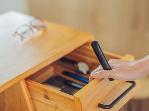 A photo of a person carrying a black RELX Essential device while closing a wooden desk drawer.