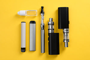 Different types of vapes lie flat on a yellow surface.