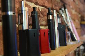 Various vape mods are lined up on a shelf.