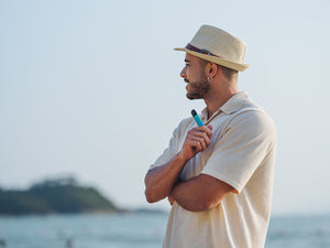 A man staring into the distance smiling as he holds a RELX vape device in his right hand.