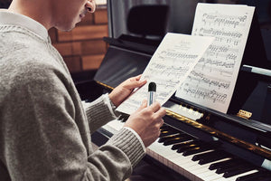 A man holding RELX Artisan in Polo Stripe while looking at a music sheet, a grand piano in front of him
