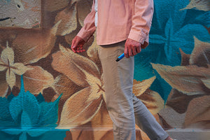 A man in salmon long sleeves and khaki pants walking while carrying a vape device.